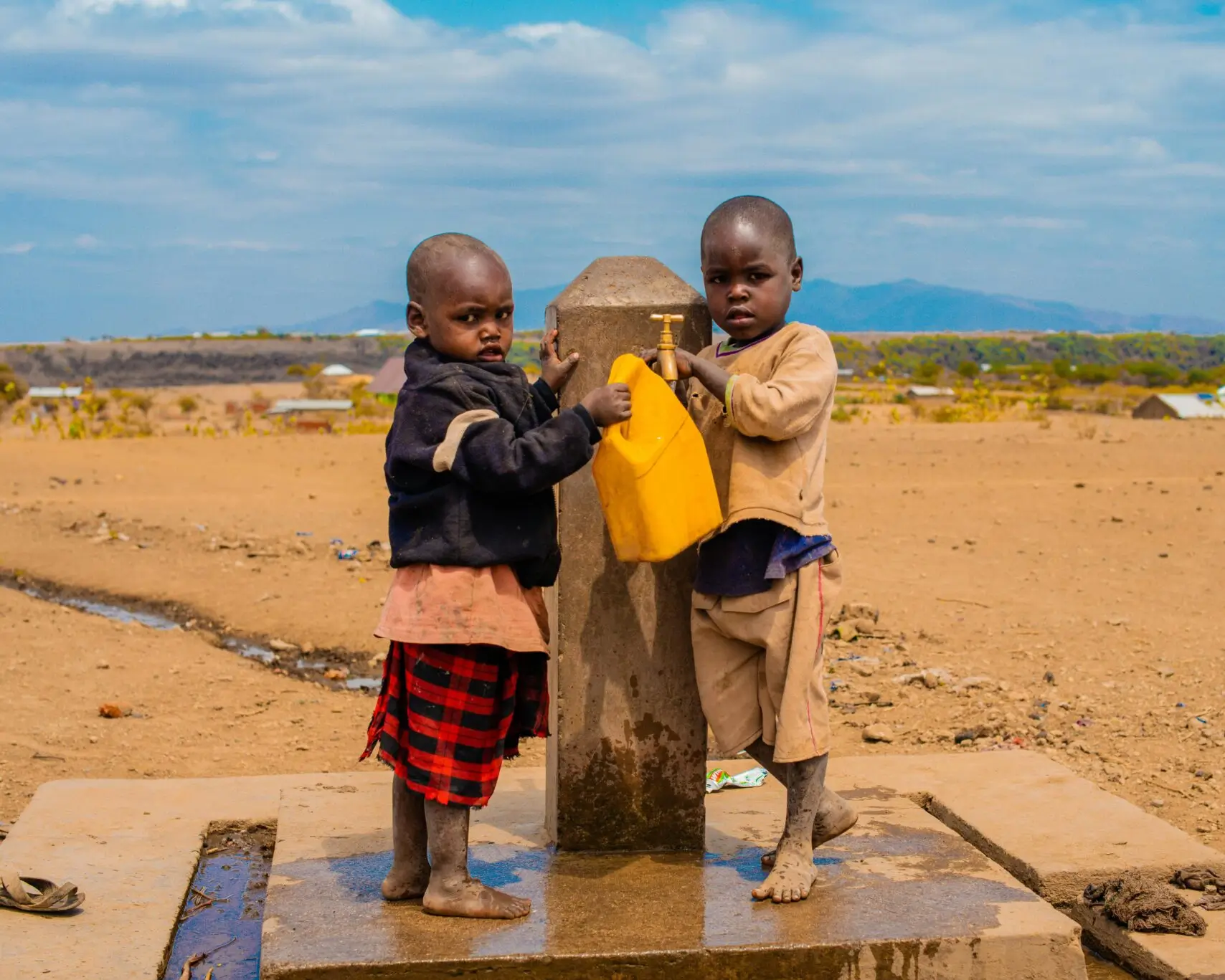 Two children at a community tap stand in a drought-affected rural community