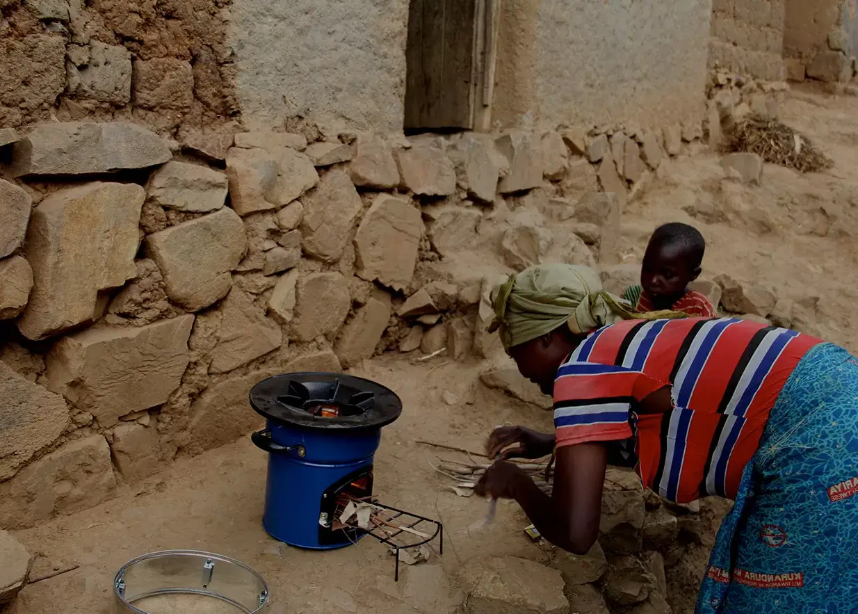 A woman using a GPI-supplied clean-burning cookstove outside her home